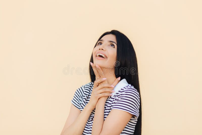 O modelo fêmea novo lindo alegre olha felizmente ascendente e mantém a mão sob o queixo, observa algo agradável, vestido em ocasi fotografia de stock O modelo fêmea novo lindo alegre olha felizmente ascendente e mantém a mão sob o queixo, observa algo agradável, vestido em ocasi fotografia de stock