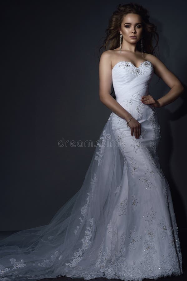 O modelo novo bonito com perfeito compõe e cabelo de sopro que veste o vestido de casamento branco do laço da sereia luxuoso com fotografia de stock royalty free O modelo novo bonito com perfeito compõe e cabelo de sopro que veste o vestido de casamento branco do laço da sereia luxuoso com fotografia de stock royalty free
