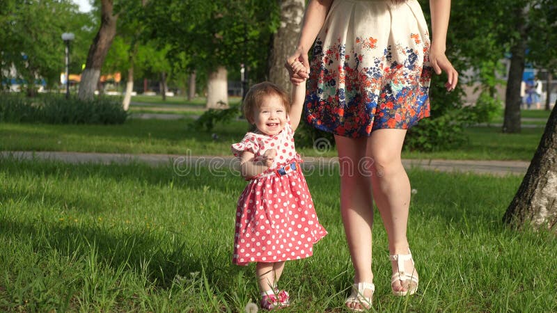 O Mum anda no parque no gramado com criança pequena, mamã ensina para andar pouca filha, criança guarda a mão de sua mãe fotografia de stock O Mum anda no parque no gramado com criança pequena, mamã ensina para andar pouca filha, criança guarda a mão de sua mãe fotografia de stock