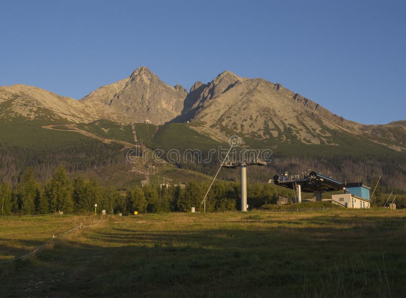 O ouro da escala de montanhas de Tatra coloriu a luz do nascer do sol, o elevador de esqui em Tatranska Lomnice com árvores verde imagens de stock O ouro da escala de montanhas de Tatra coloriu a luz do nascer do sol, o elevador de esqui em Tatranska Lomnice com árvores verde imagens de stock