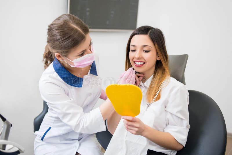 O paciente e o dentista felizes novos com ponta de prova estão verificando os dentes no espelho após o procedimento dental no esc fotografia de stock royalty free O paciente e o dentista felizes novos com ponta de prova estão verificando os dentes no espelho após o procedimento dental no esc fotografia de stock royalty free