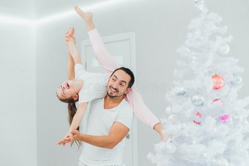 O pai brinca com a filha perto da árvore de Natal imagens de stock royalty free O pai brinca com a filha perto da árvore de Natal imagens de stock royalty free