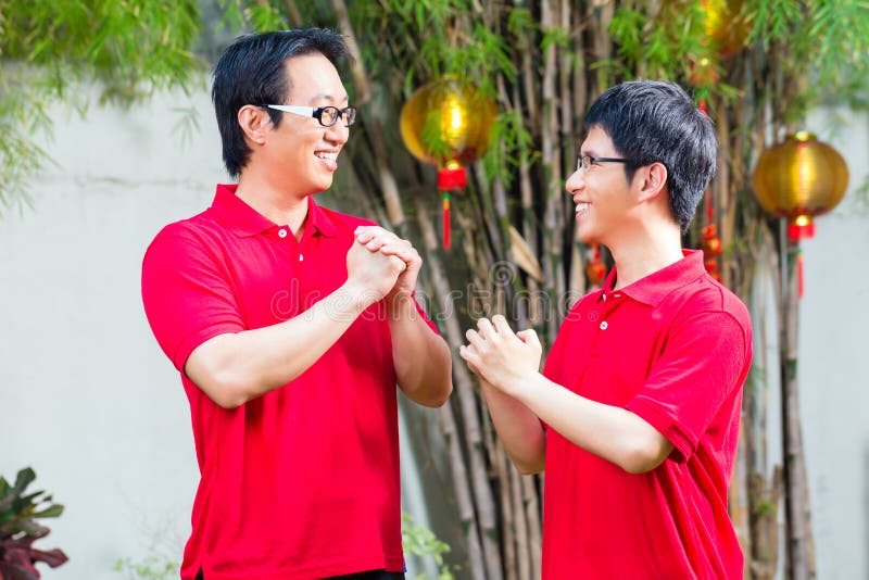 Father and adult son celebrating Chinese new year traditional greeting, wearing red shirts. Father and adult son celebrating Chinese new year traditional greeting, wearing red shirts