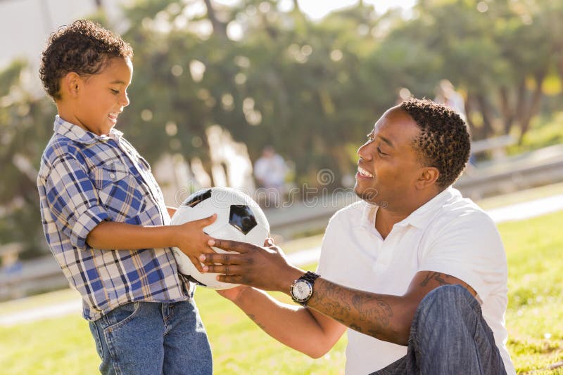 African American Father Hands New Soccer Ball to Mixed Race Son at the Park. African American Father Hands New Soccer Ball to Mixed Race Son at the Park.