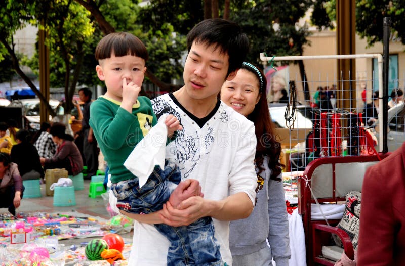 Father walking in New Square carries his young, nose-picking little boy who sports a bowl-cut haircut in Pengzhou, China. Father walking in New Square carries his young, nose-picking little boy who sports a bowl-cut haircut in Pengzhou, China.