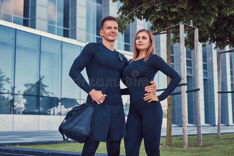 O par feliz da aptidão em um sportswear, em uma menina loura 'sexy' e em um indivíduo muscular considerável está na cidade modern fotos de stock O par feliz da aptidão em um sportswear, em uma menina loura 'sexy' e em um indivíduo muscular considerável está na cidade modern fotos de stock