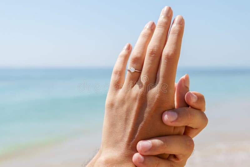 O par feliz novo está obtendo contratou na proposta do casamento na praia fotografia de stock royalty free O par feliz novo está obtendo contratou na proposta do casamento na praia fotografia de stock royalty free