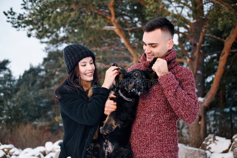 O par romântico bonito está tendo o divertimento com seu cão fora no dia de inverno imagem de stock O par romântico bonito está tendo o divertimento com seu cão fora no dia de inverno imagem de stock
