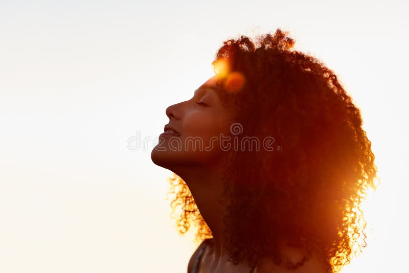 O perfil de uma mulher com afro silhoutted contra o sol da noite