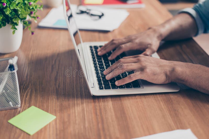 O perfil lateral colheu a foto das mãos afro-americanas do homem de negócios do ` s no teclado do portátil em um desktop de madei imagens de stock