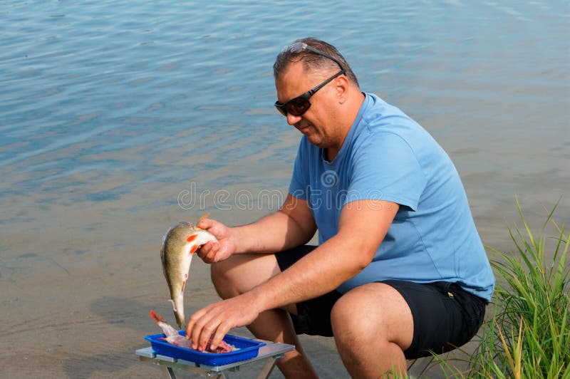 O pescador corta os peixes na costa, um homem limpa os peixes fotografia de stock O pescador corta os peixes na costa, um homem limpa os peixes fotografia de stock