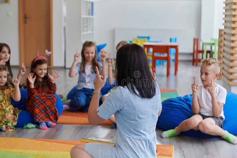 O profesoară fericită stând și jucând jocuri de mână cu un grup de elevi.