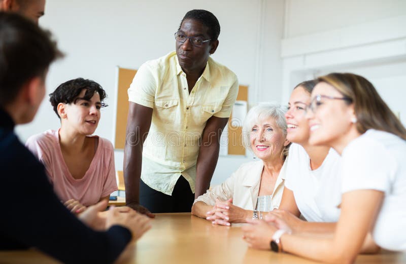 O professor macho africano, juntamente com alunos de diferentes idades, conduz aulas intensivas em mesas redondas em foto de stock