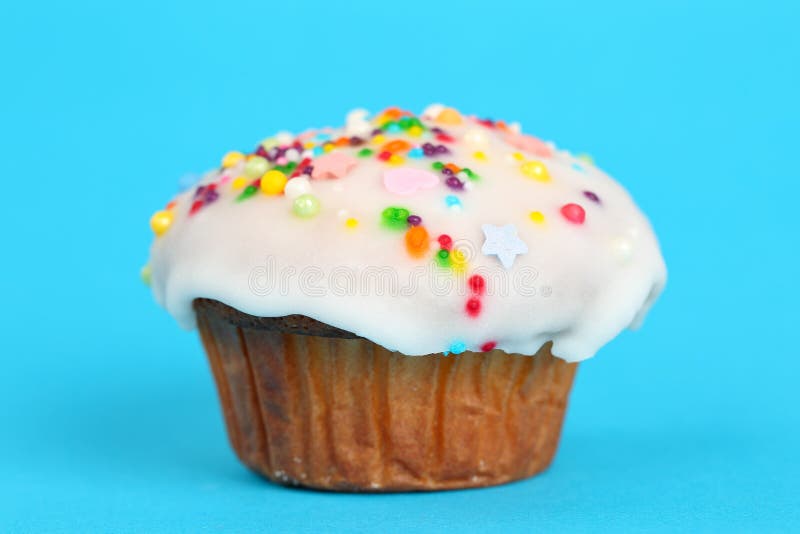 O queque caseiro delicioso com crosta de gelo branca do fundente e açúcar colorido polvilha em um fundo brilhante do azul de turq imagem de stock royalty free O queque caseiro delicioso com crosta de gelo branca do fundente e açúcar colorido polvilha em um fundo brilhante do azul de turq imagem de stock royalty free