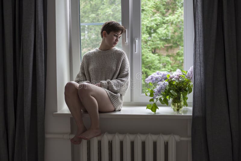O ramalhete dos galhos lilás em um frasco transparente na cadeira branca como uma decoração do interior A menina senta-se na jane imagem de stock O ramalhete dos galhos lilás em um frasco transparente na cadeira branca como uma decoração do interior A menina senta-se na jane imagem de stock