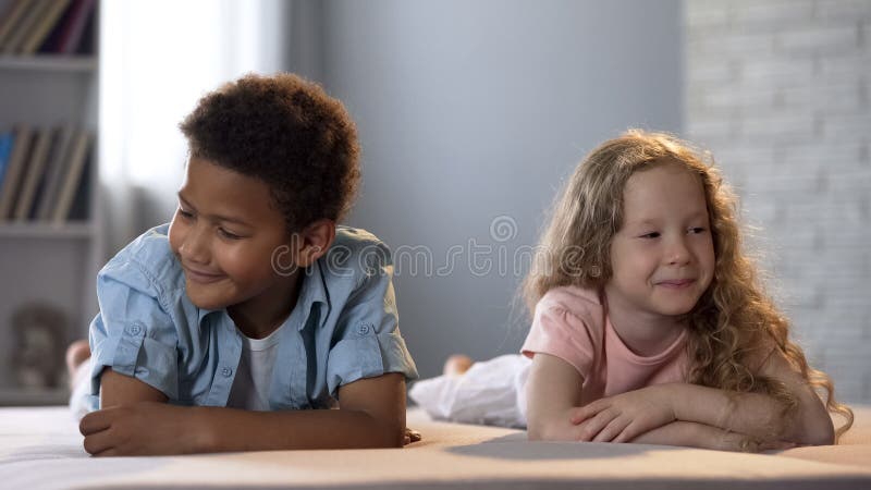 O rapaz pequeno e a menina gerenciem timidamente afastado que sorri, sentimento da infância, amor imagem de stock royalty free O rapaz pequeno e a menina gerenciem timidamente afastado que sorri, sentimento da infância, amor imagem de stock royalty free