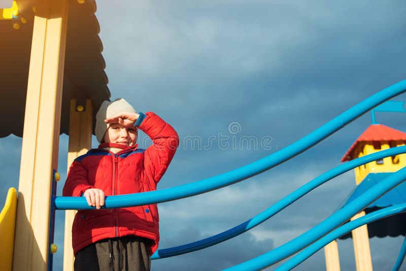 O rapaz pequeno joga no campo de jogos do ar livre no dia frio Infância feliz Campo de jogos colorido moderno no fundo do céu neb fotografia de stock O rapaz pequeno joga no campo de jogos do ar livre no dia frio Infância feliz Campo de jogos colorido moderno no fundo do céu neb fotografia de stock