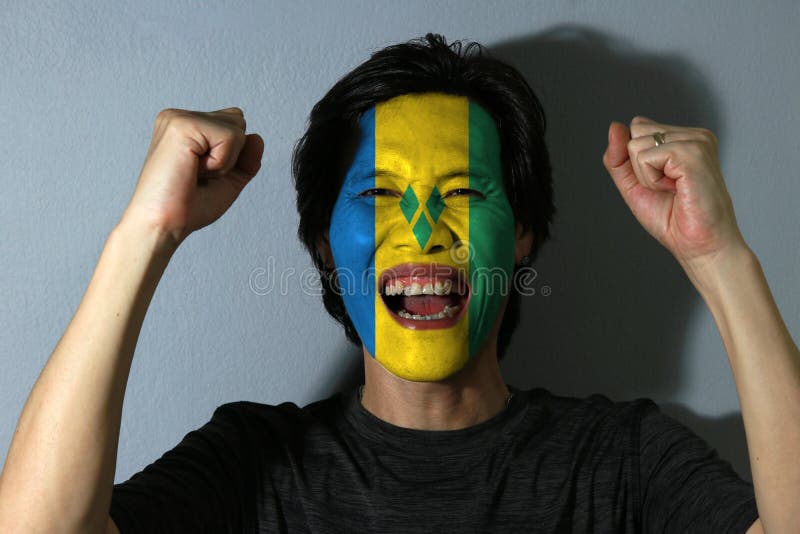 O retrato alegre de um homem com a bandeira de Saint Vincent pintou em sua cara no fundo cinzento O conceito do esporte ou do nac imagem de stock O retrato alegre de um homem com a bandeira de Saint Vincent pintou em sua cara no fundo cinzento O conceito do esporte ou do nac imagem de stock