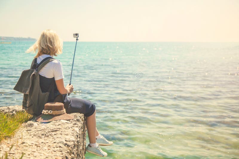 O retrato bonito do selfie das tomadas do turista da jovem mulher no litoral em uma menina de dia ensolarado toma a foto para o b imagens de stock O retrato bonito do selfie das tomadas do turista da jovem mulher no litoral em uma menina de dia ensolarado toma a foto para o b imagens de stock