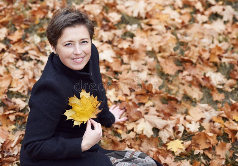O retrato da jovem mulher, sentando-se no fundo amarelo das folhas, vestiu-se no revestimento preto, estação do outono, parque da foto de stock O retrato da jovem mulher, sentando-se no fundo amarelo das folhas, vestiu-se no revestimento preto, estação do outono, parque da foto de stock