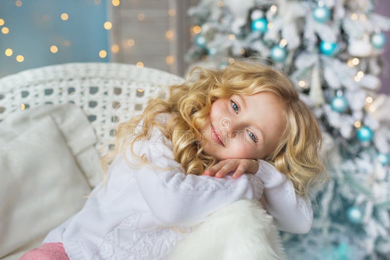 O retrato da menina bonita senta-se e sonha-se em uma cadeira no tempo do Natal imagem de stock O retrato da menina bonita senta-se e sonha-se em uma cadeira no tempo do Natal imagem de stock