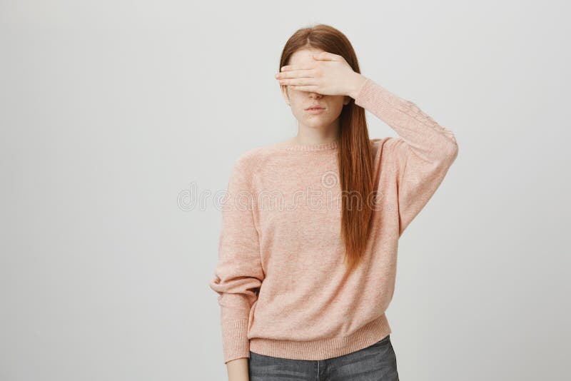O retrato da menina europeia nova do gengibre que é calma e séria, cobrindo eyes com mão, pulôver na moda vestindo e foto de stock royalty free O retrato da menina europeia nova do gengibre que é calma e séria, cobrindo eyes com mão, pulôver na moda vestindo e foto de stock royalty free
