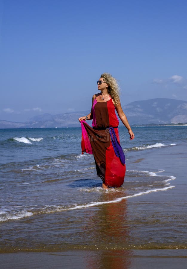 Lady in bright elegant red dress at beach, with sea and blue sky as background. Lady in bright elegant red dress at beach, with sea and blue sky as background.