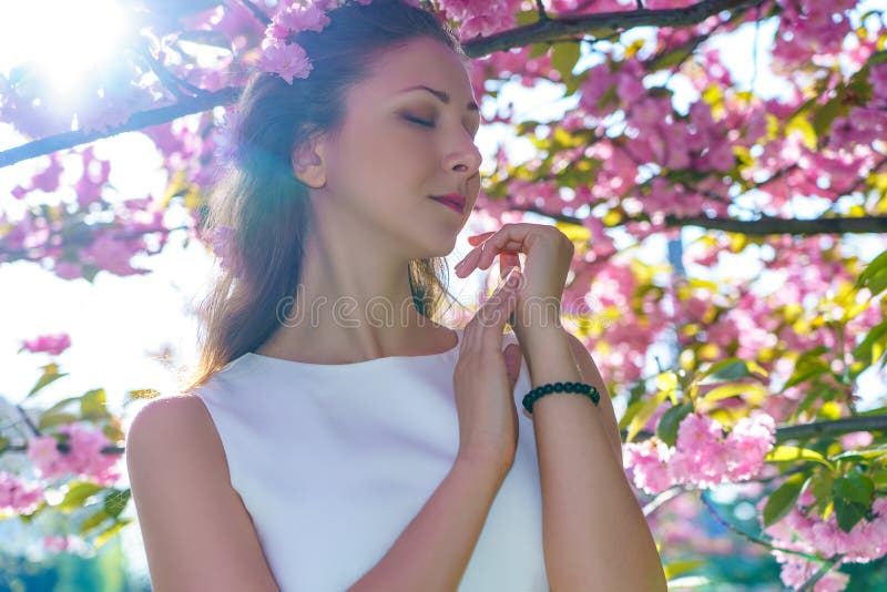 O retrato da mulher bonita nova com as flores cor-de-rosa em seu cabelo está no vestido branco levanta a proposta na árvore de sa fotos de stock royalty free O retrato da mulher bonita nova com as flores cor-de-rosa em seu cabelo está no vestido branco levanta a proposta na árvore de sa fotos de stock royalty free