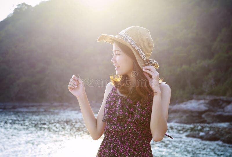 O retrato da mulher bonita nova que veste o vestido longo e o chapéu de palha largo que sorri no uso do lugar do lado de mar para foto de stock O retrato da mulher bonita nova que veste o vestido longo e o chapéu de palha largo que sorri no uso do lugar do lado de mar para foto de stock