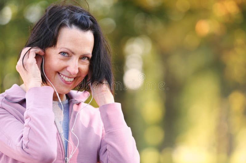 O retrato da mulher idosa prepara-se para movimentar-se com os fones de ouvido no parque fotografia de stock royalty free O retrato da mulher idosa prepara-se para movimentar-se com os fones de ouvido no parque fotografia de stock royalty free