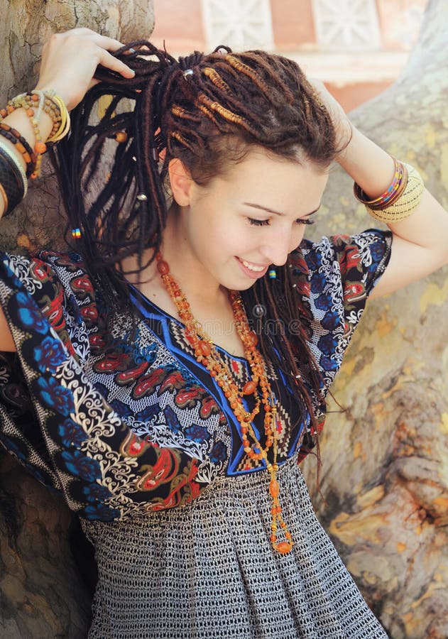 O retrato de sorriso novo da mulher com dreadlocks vestiu-se no vestido decorativo do estilo do boho imagens de stock royalty free O retrato de sorriso novo da mulher com dreadlocks vestiu-se no vestido decorativo do estilo do boho imagens de stock royalty free