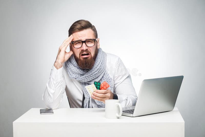O retrato do homem novo cansado insalubre na camisa branca, o lenço e o traje de cerimônia estão sentando-se no escritório e na n fotografia de stock O retrato do homem novo cansado insalubre na camisa branca, o lenço e o traje de cerimônia estão sentando-se no escritório e na n fotografia de stock
