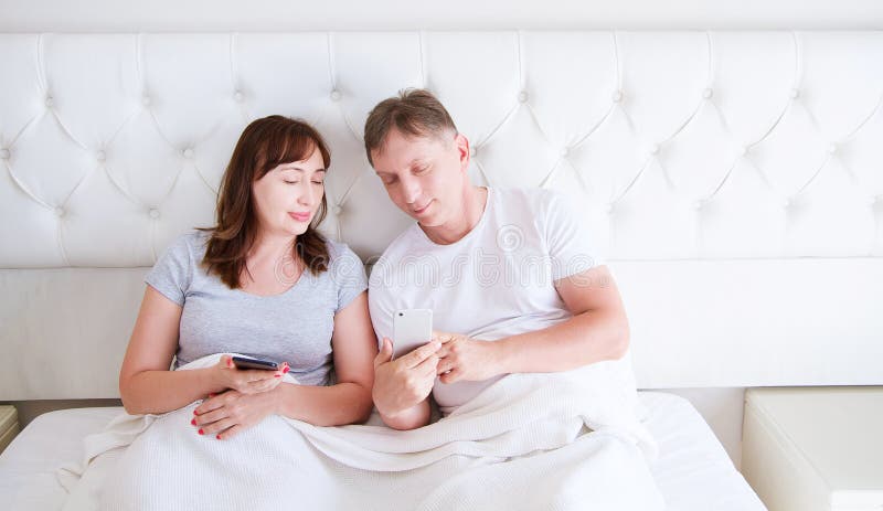 O retrato do meio de amor envelheceu os pares que sorriem e que olham algo em um telefone celular no quarto foto de stock O retrato do meio de amor envelheceu os pares que sorriem e que olham algo em um telefone celular no quarto foto de stock