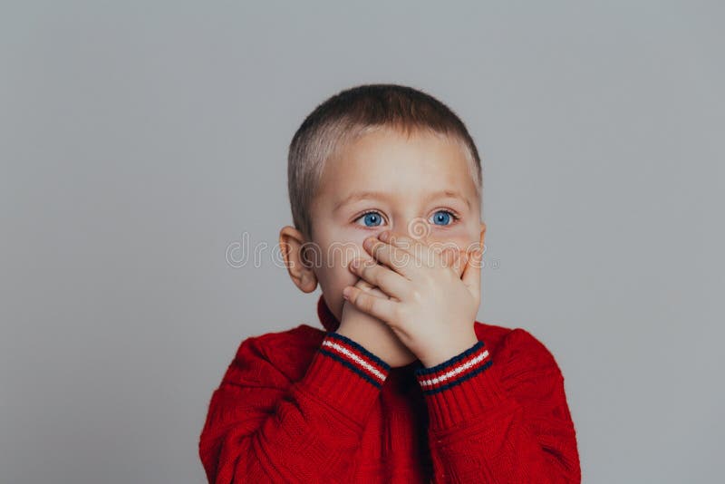 O retrato do menino atrativo na camiseta vermelha que cobre sua boca com as mãos fecha-se acima imagem de stock royalty free O retrato do menino atrativo na camiseta vermelha que cobre sua boca com as mãos fecha-se acima imagem de stock royalty free