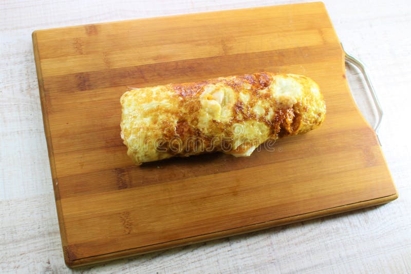 O rolo da omeleta dos ovos fritos encheu-se com o queijo e o abobrinha com o fundo de madeira branco fotografia de stock O rolo da omeleta dos ovos fritos encheu-se com o queijo e o abobrinha com o fundo de madeira branco fotografia de stock