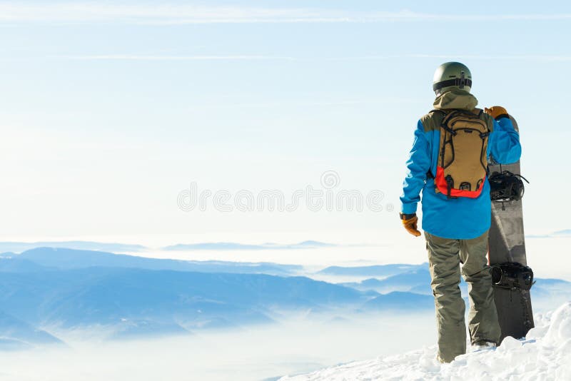 O snowboarder novo no capacete que está ao lado do snowboard empurrou na neve com cenário bonito no fundo fotografia de stock royalty free O snowboarder novo no capacete que está ao lado do snowboard empurrou na neve com cenário bonito no fundo fotografia de stock royalty free
