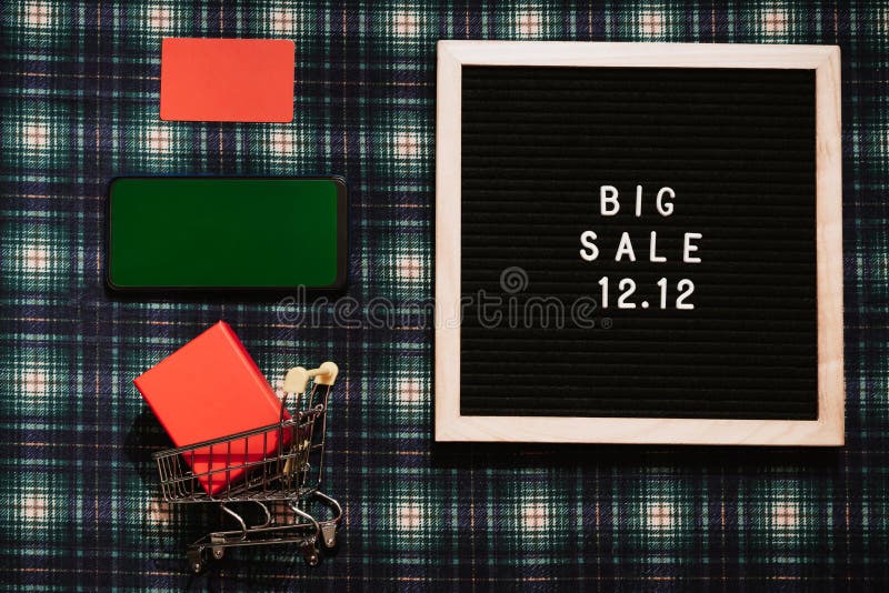 The text of the 12.12 sale is on a letter board with a gift box, a credit card, a mini grocery cart and a phone with a chrome screen. Design to promote the winter sale at the end of the year. Top view. The text of the 12.12 sale is on a letter board with a gift box, a credit card, a mini grocery cart and a phone with a chrome screen. Design to promote the winter sale at the end of the year. Top view