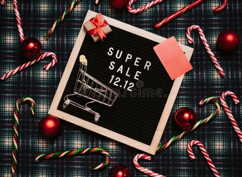 The text of the sale 12.12 on a letter board with a red gift box and Christmas candies, a credit card and a mini grocery cart. Design to promote the winter sale at the end of the year. Top view. The text of the sale 12.12 on a letter board with a red gift box and Christmas candies, a credit card and a mini grocery cart. Design to promote the winter sale at the end of the year. Top view