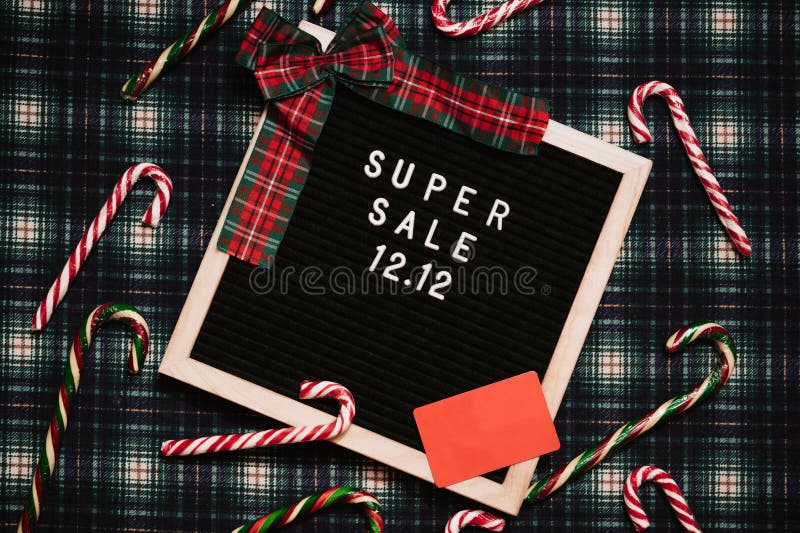The text of the sale 12.12 on a letter board with a red gift box and Christmas candies, a credit card and a mini grocery cart. Design to promote the winter sale at the end of the year. Top view. The text of the sale 12.12 on a letter board with a red gift box and Christmas candies, a credit card and a mini grocery cart. Design to promote the winter sale at the end of the year. Top view