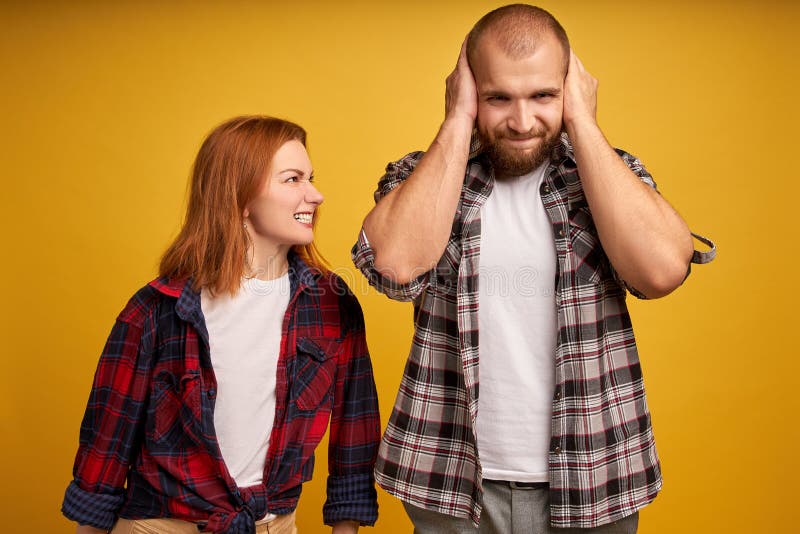 O tiro da mulher vermelha irritada irritada do cabelo censura o marido, acusa em algo gritos com aborrecimento, homem não barbead imagem de stock royalty free O tiro da mulher vermelha irritada irritada do cabelo censura o marido, acusa em algo gritos com aborrecimento, homem não barbead imagem de stock royalty free