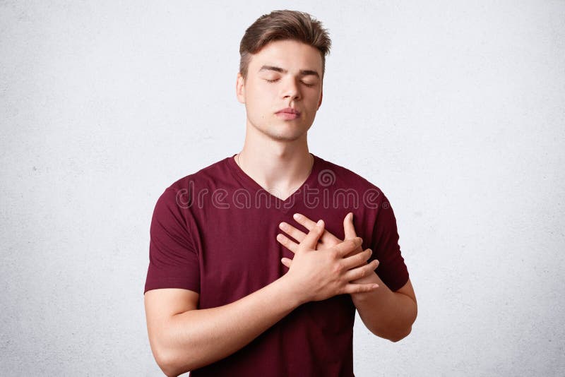O tiro isolado do homem grato satisfeito com corpo forte, mantém as mãos na caixa, olhos fechados, tem o penteado na moda, poses foto de stock O tiro isolado do homem grato satisfeito com corpo forte, mantém as mãos na caixa, olhos fechados, tem o penteado na moda, poses foto de stock