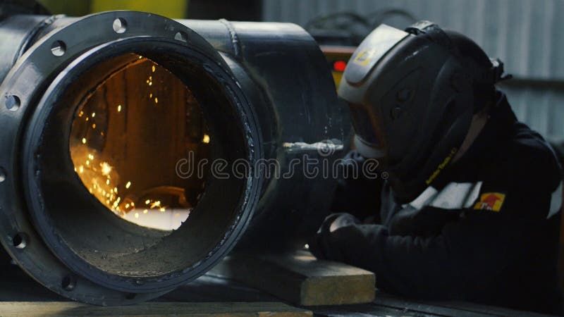 O trabalhador com a máscara da soldadura dentro da fábrica O processo da soldadura de uma peça do equipamento dentro da fábrica