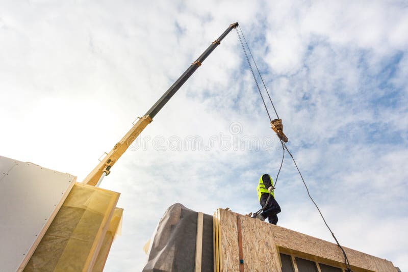 O trabalhador do construtor do Roofer com o guindaste que instala os painéis isolados estruturais SORVE Casa energia-eficiente de imagens de stock royalty free O trabalhador do construtor do Roofer com o guindaste que instala os painéis isolados estruturais SORVE Casa energia-eficiente de imagens de stock royalty free
