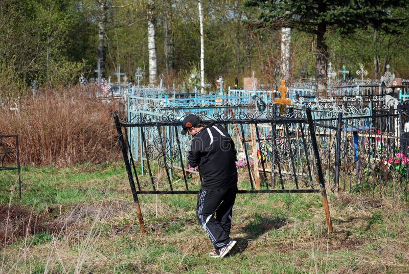 O trabalhador põe um ogradka no cemitério rural na primavera fotografia de stock O trabalhador põe um ogradka no cemitério rural na primavera fotografia de stock