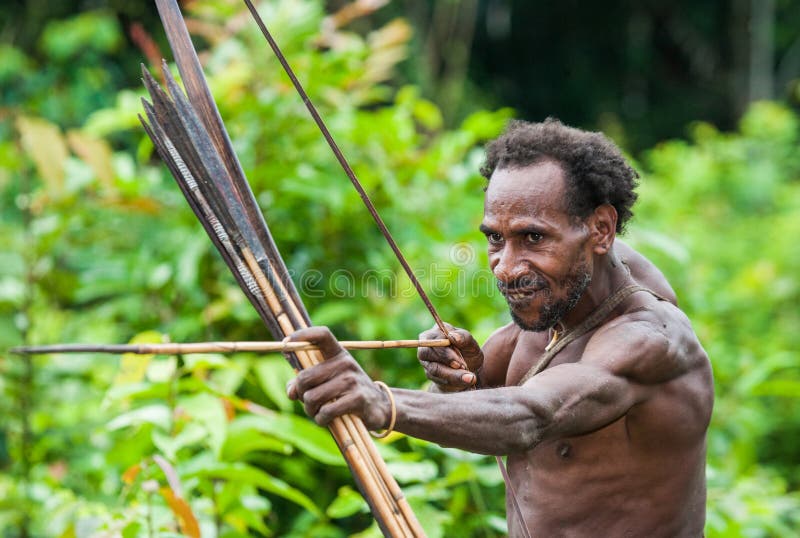 INDONESIA, ONNI VILLAGE, NEW GUINEA - JUNE 24: Man Korowai tribe shoots a bow. Tribe of Korowai Kombai , Kolufo. INDONESIA, ONNI VILLAGE, NEW GUINEA - JUNE 24: Man Korowai tribe shoots a bow. Tribe of Korowai Kombai , Kolufo.