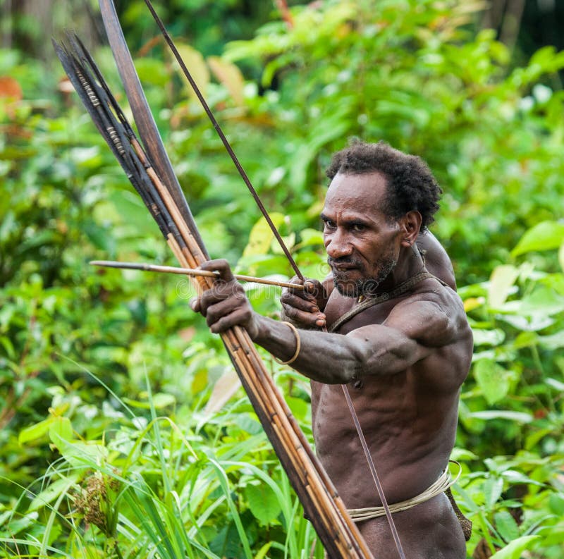 INDONESIA, ONNI VILLAGE, NEW GUINEA - JUNE 24: Man Korowai tribe shoots a bow. Tribe of Korowai Kombai , Kolufo. INDONESIA, ONNI VILLAGE, NEW GUINEA - JUNE 24: Man Korowai tribe shoots a bow. Tribe of Korowai Kombai , Kolufo.