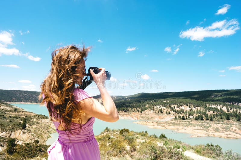 O turista fêmea de cabelos compridos em um vestido cor-de-rosa com uma câmera está nas montanhas fotos de stock royalty free O turista fêmea de cabelos compridos em um vestido cor-de-rosa com uma câmera está nas montanhas fotos de stock royalty free