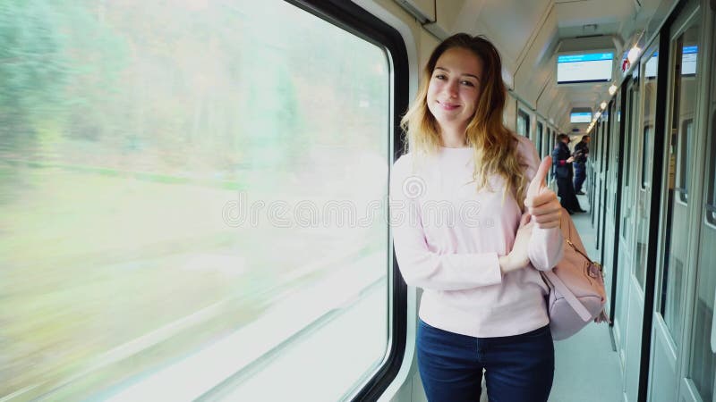 O turista fêmea novo aprecia viajar e viajar, mostra o gesto e está perto da grande janela no trem