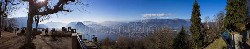 O turista que admira a cidade dos cumes, do lago lugano e da Lugano de uma vigia aponta na montagem Bre foto de stock royalty free O turista que admira a cidade dos cumes, do lago lugano e da Lugano de uma vigia aponta na montagem Bre foto de stock royalty free