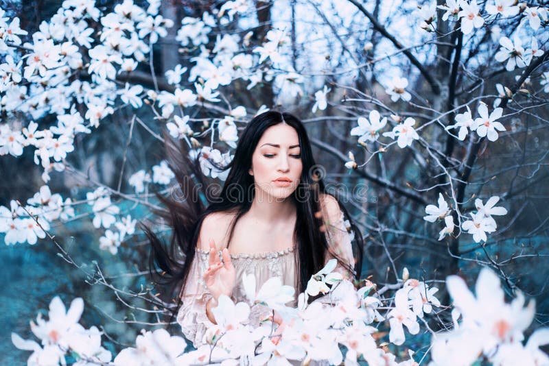 O tânără încântătoare cu ochi închiși stă în grădina magnoliilor înfloriți. părul se ridică în sus stock photography